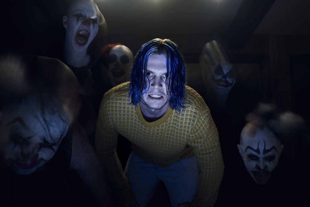 Evan Peters in season 7 of AHS, with blue hair and pale skin. He is surrounded by shadowed figures. 