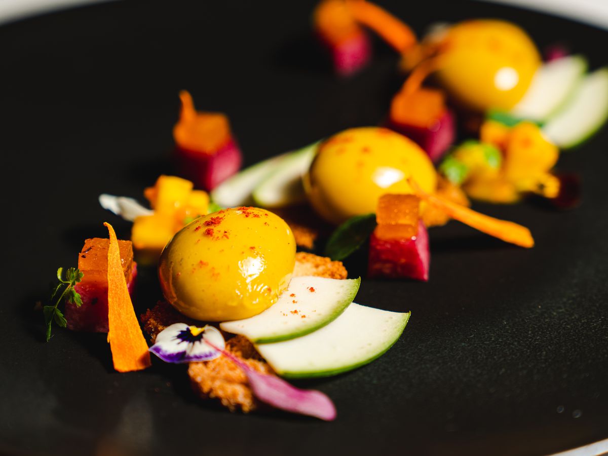 A colorful salad with edible flowers, sliced apples, and dollops of mango cream.