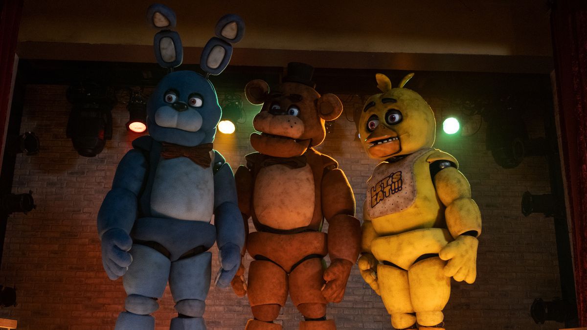 Animatronics Bonnie, Freddy Fazbear, and Chica stand on a stage, looking to the right, in the Universal Pictures movie adaptation Five Nights at Freddy’s