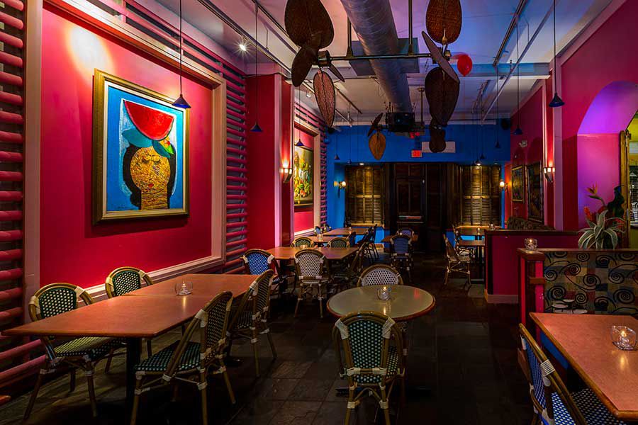 A restaurant interior features bold pink walls, bright blue accents, and colorful art.