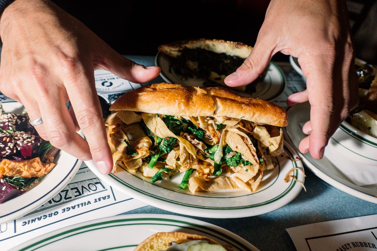 A hand grabs for a sandwich overflowing with greens and tofu skin.