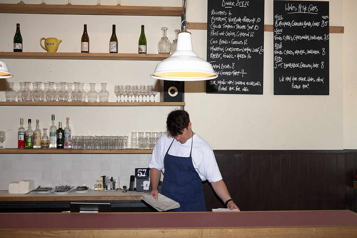 A man in a blue apron stands behind a bar