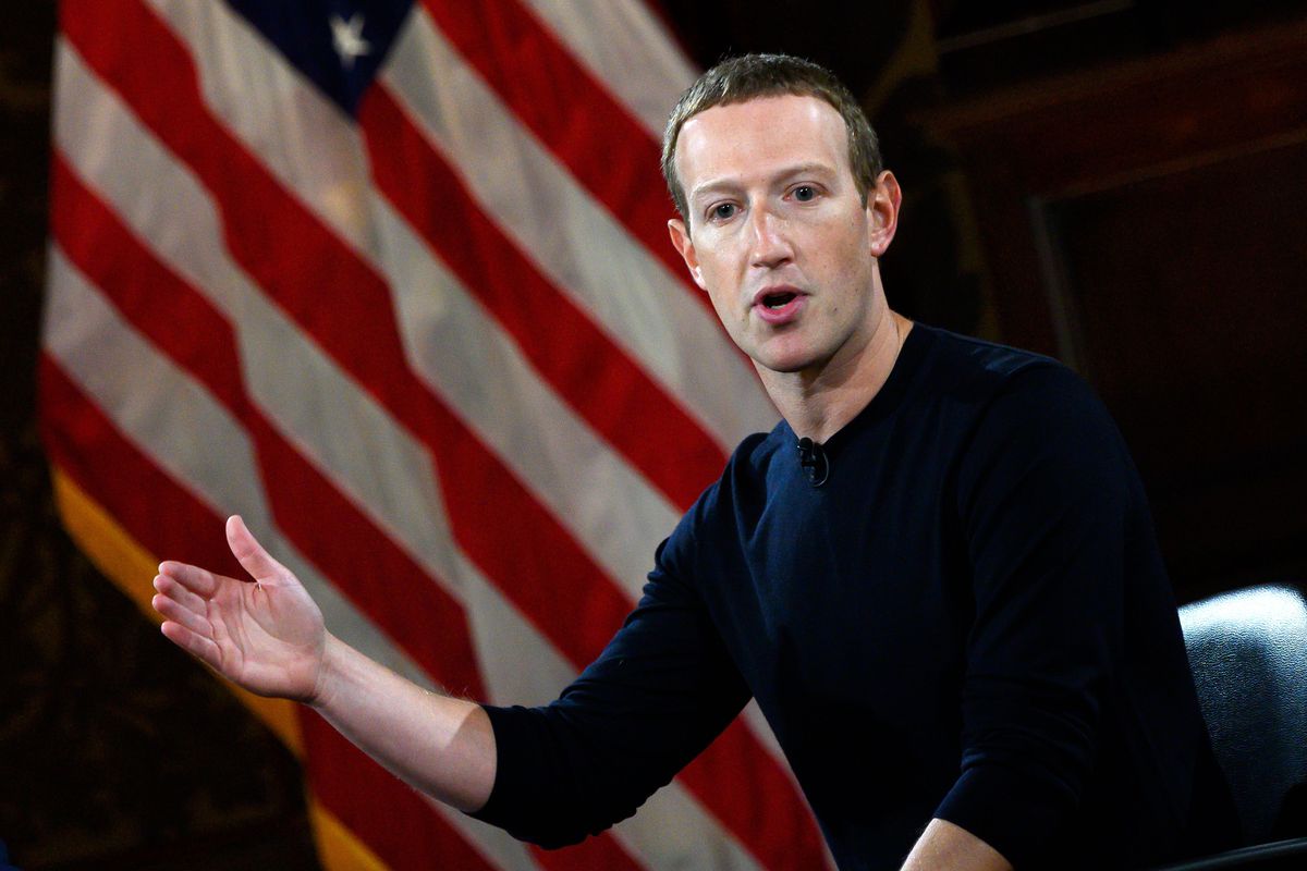 Facebook CEO Mark Zuckerberg speaking and gesturing onstage in front of an American flag.