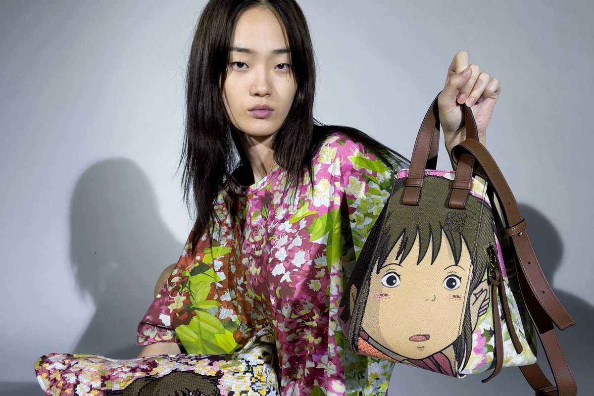 An Asian woman wearing the Loewe Spirited Away collaboration shirt holding a matching handbag and pillow