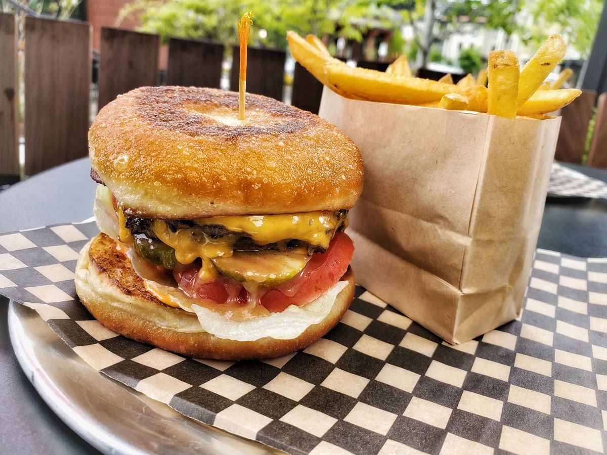 A cheeseburger is shown on a checkered paper next to a small brown bag of fries.