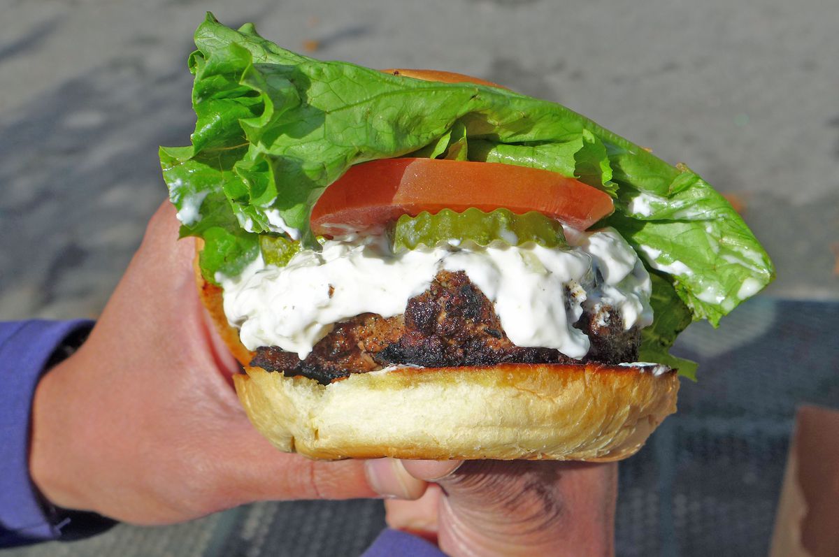A blackened patty in a bun with bright green lettuce and slice of tomato sticking out.