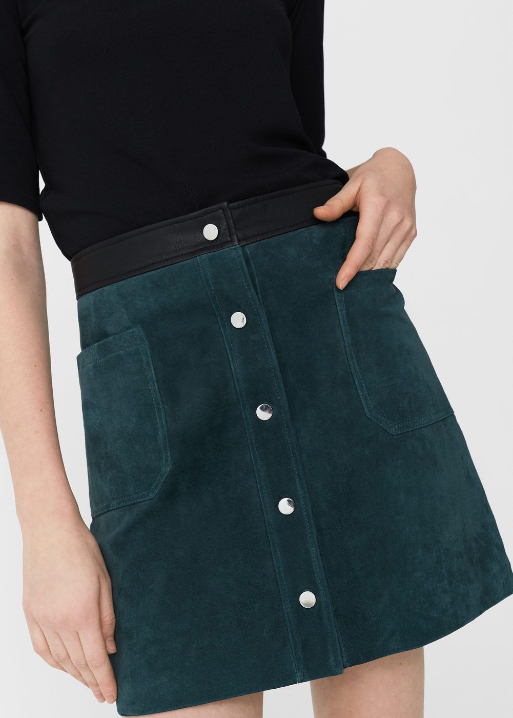 A close up of a model wearing a green suede skirt with buttons down the front