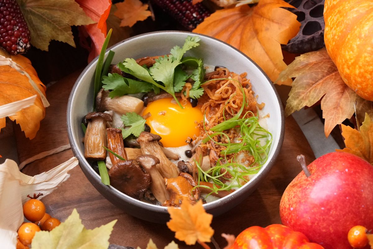 A fall tablescape with leaves and pumpkins surrounding a bowl of congee topped with an egg and wild mushrooms.