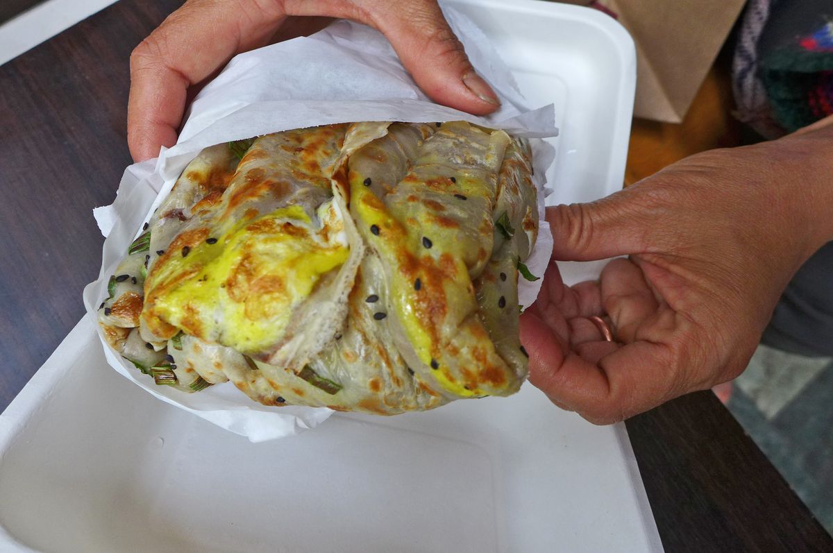 Two hands hold a stuffed flatbread with a yellowish cast.