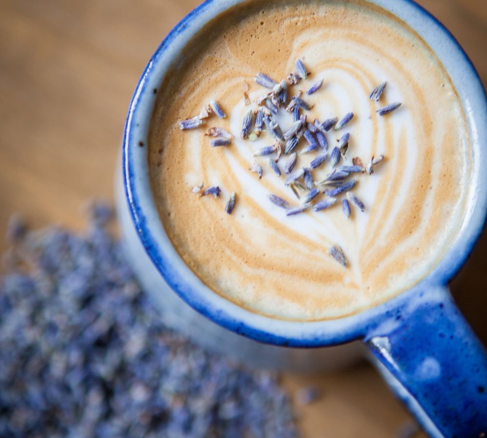 Overhead shot of a blue mug of coffee with heart-shaped foam lattee art and lavender buds.