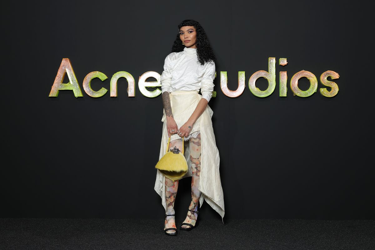 A woman in a dress in front of a sign reading Acne Studios.