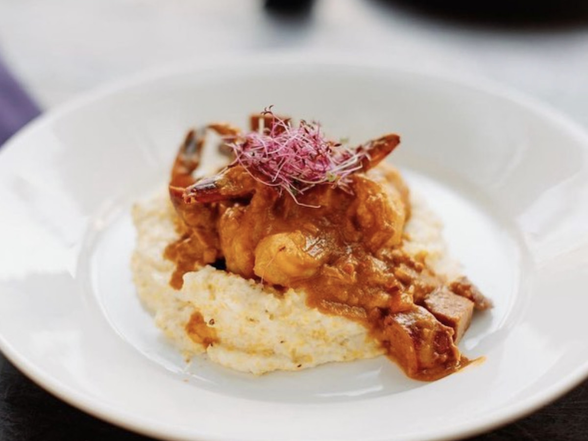A white plate with spicy shrimp on top of seasoned grits.