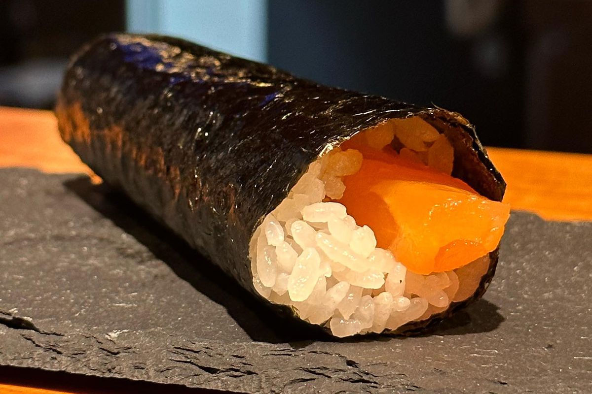 A long sushi roll with rice and pink fish.