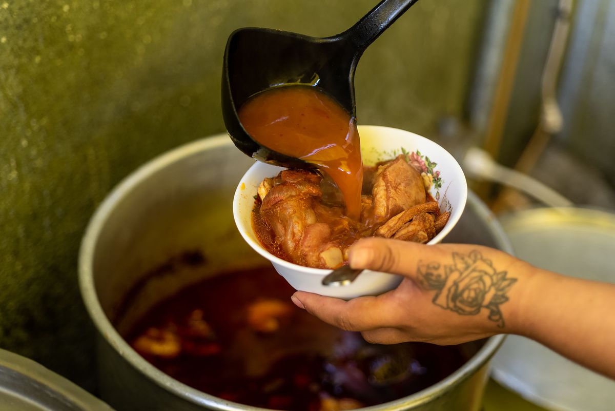 A hand holds up a bowl that consomme is being labeled into.