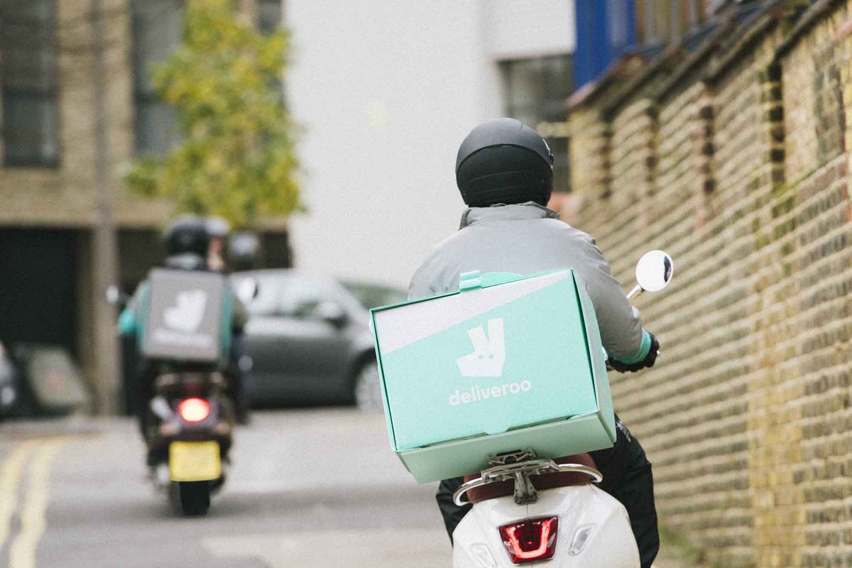 A Deliveroo rider in a Deliveroo jacket rides a motorbike in London
