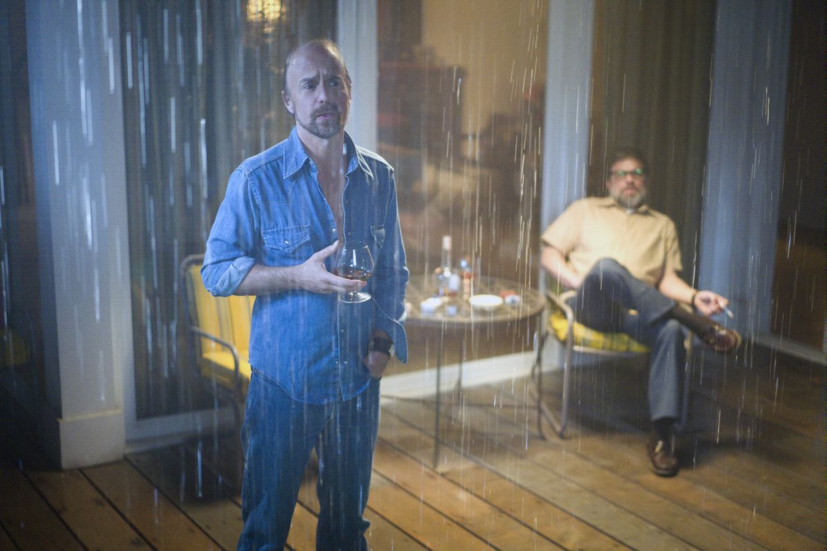 A scene from the FX show “Fosse/Verdon” where two characters are outside drinking brandy on the deck of a beach house in the rain.