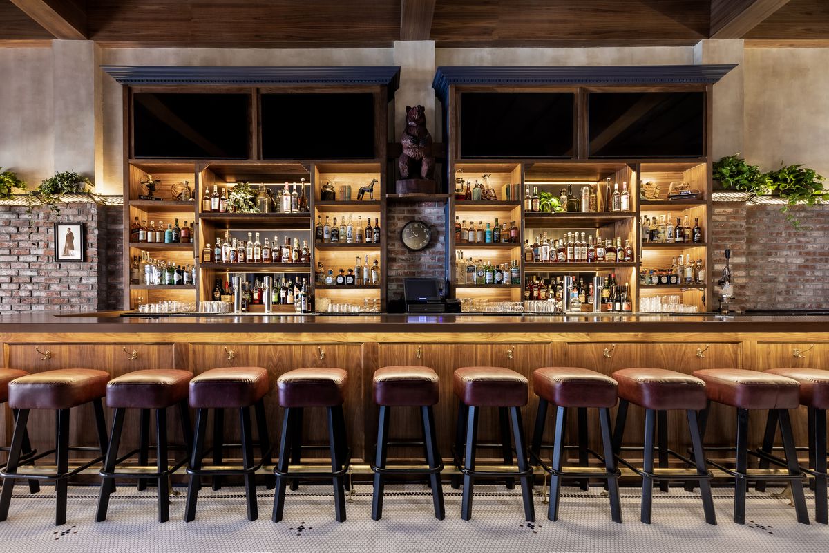 A bar with leather stools and back-lit shelving.