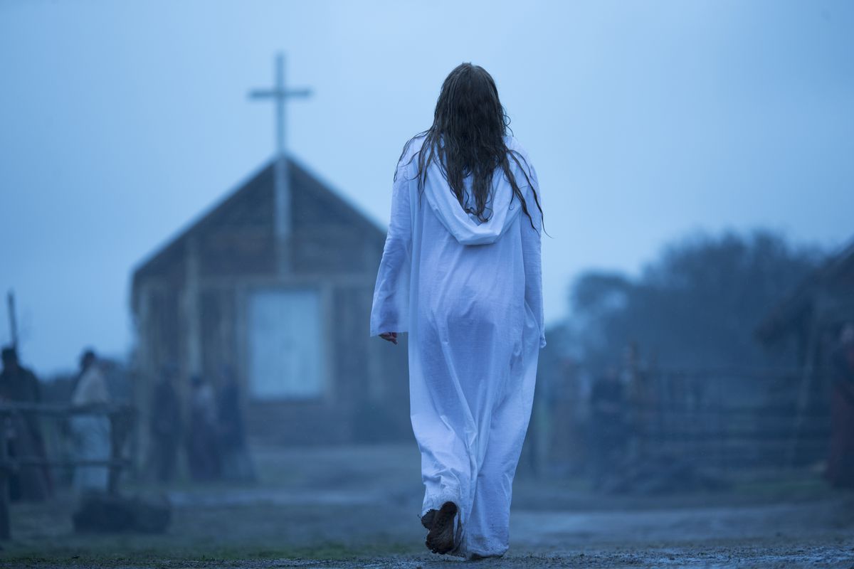 A woman in a white robe walks toward a church.
