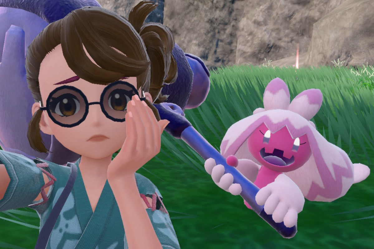 Tinkaton standing behind a trainer taking a selfie. The trainer has a worried look on her face.