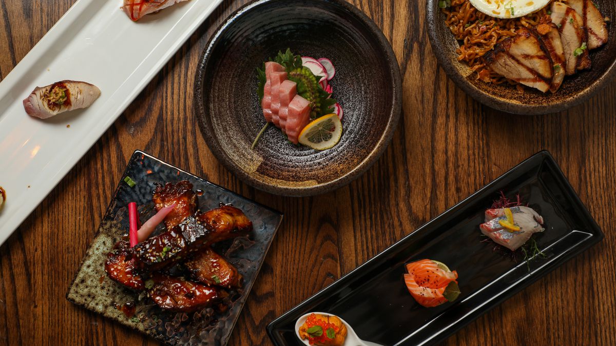 Overhead shot of a plate with three pieces of dressed nigiri, a plate of pork short ribs, a bowl of otoro sashimi, a bowl of sha-su ramen, and a plate of three pieces of sashimi.