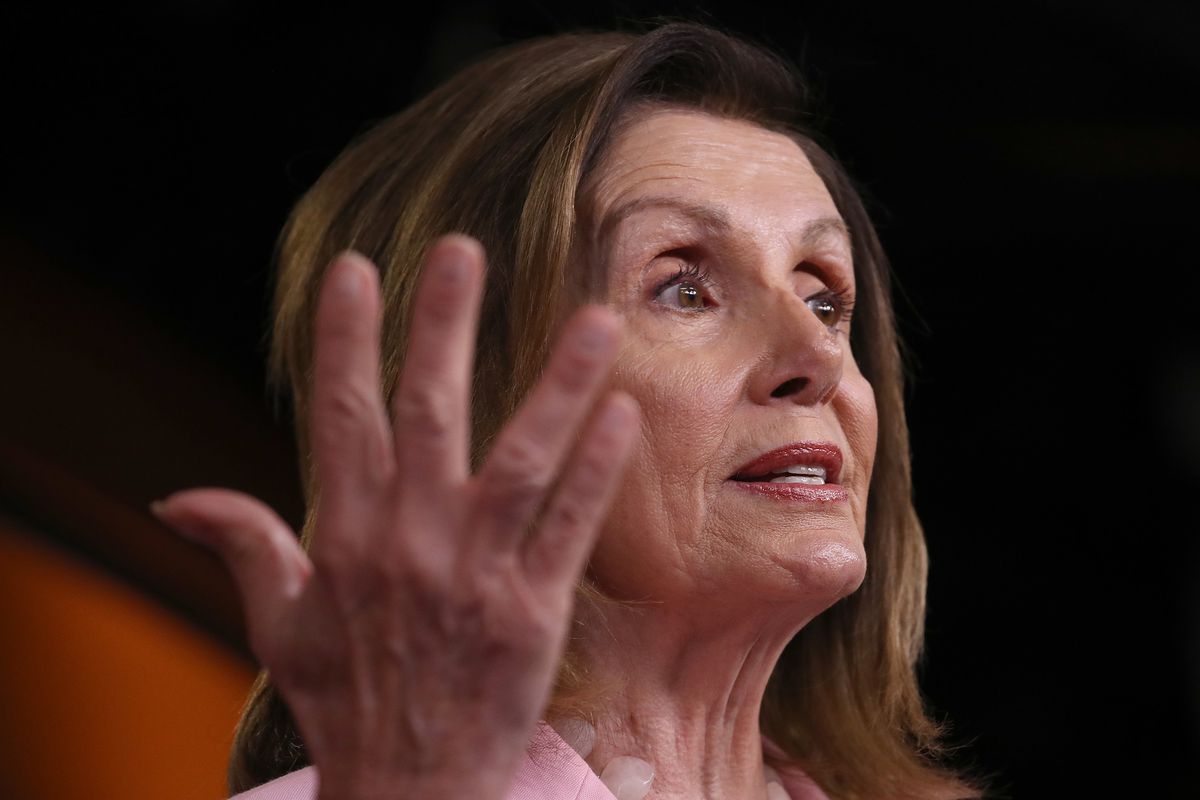 Pelosi gestures at a podium in a pink suit. 