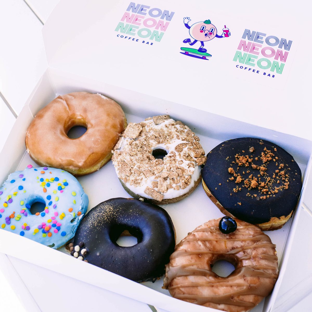 A box of colorful doughnuts in a box with a logo that’s a cartoon doughnut