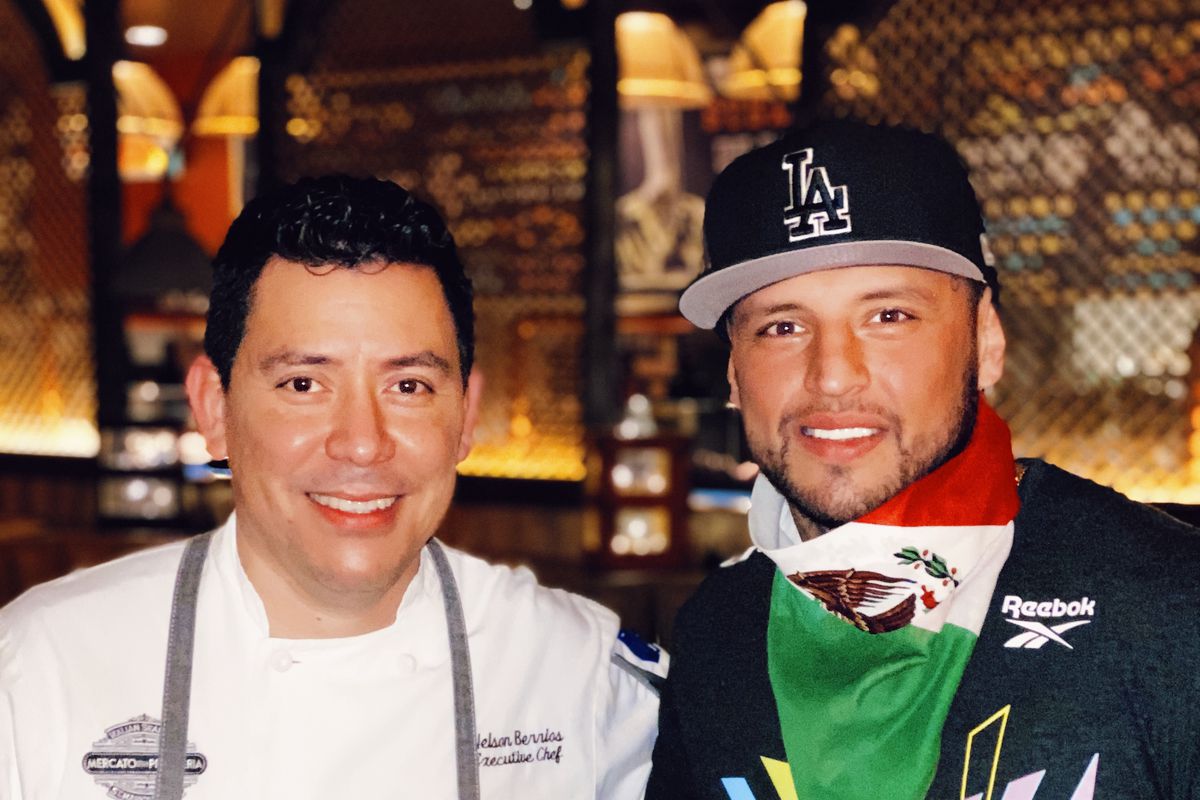 A chef in a white jacket stands next to a man with a Mexican flag scarf around his neck