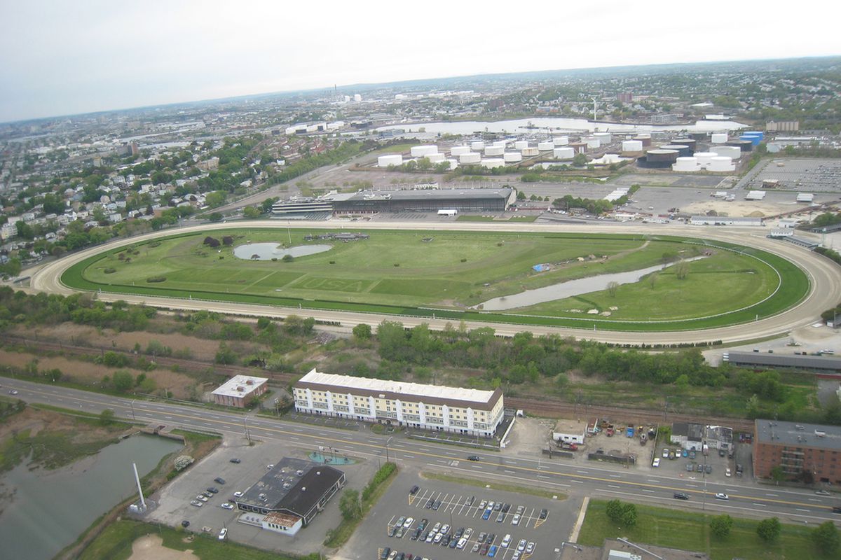 An aerial view of a large park space. There are buildings on the perimeter of the park space.