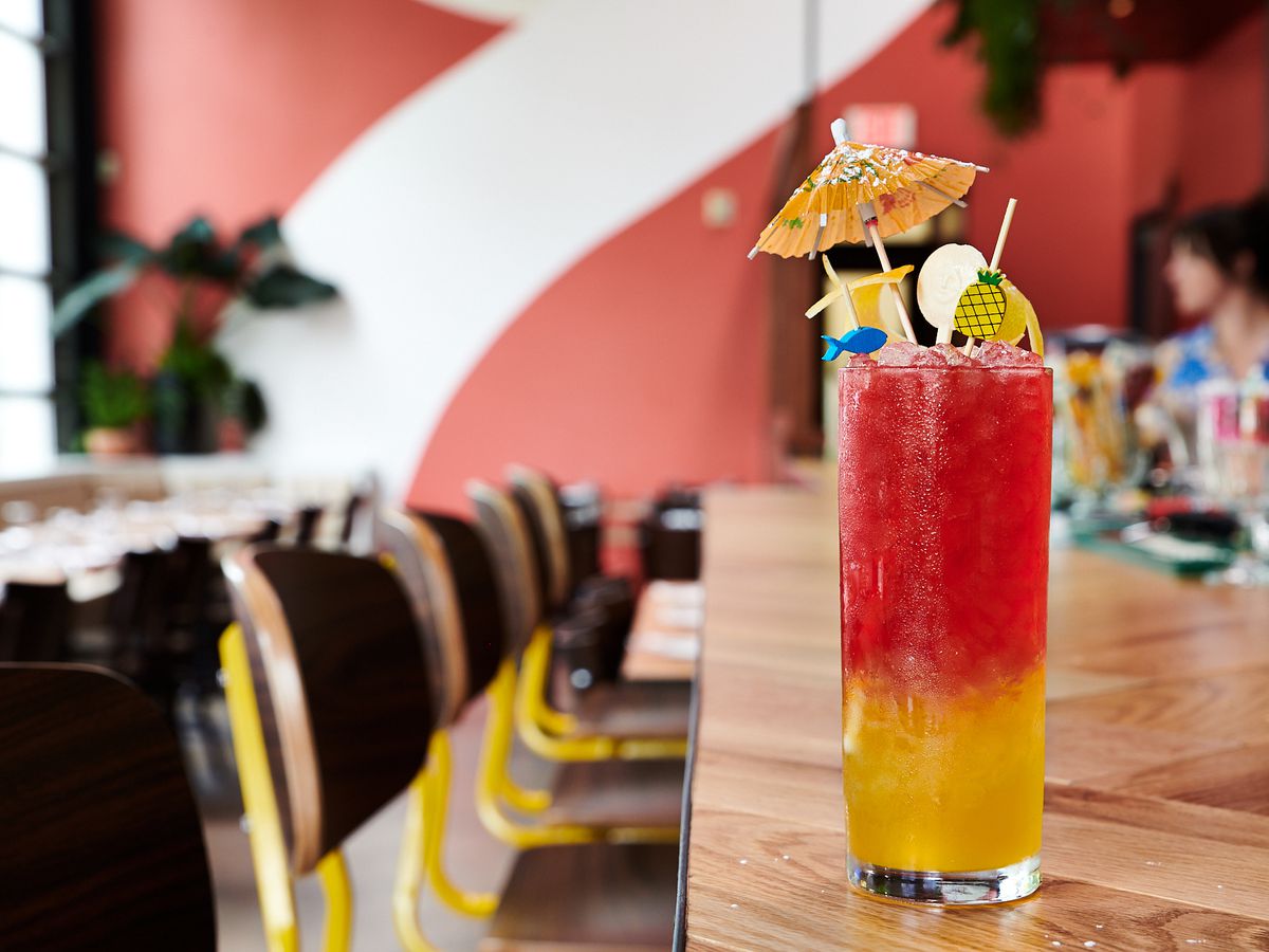 A pink and yellow cocktail with umbrellas sits on the bar at Eem
