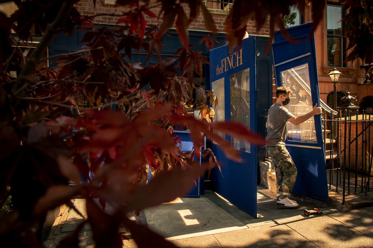 A person is standing outside, taking down one side of an outdoor vestibule in front of a restaurant