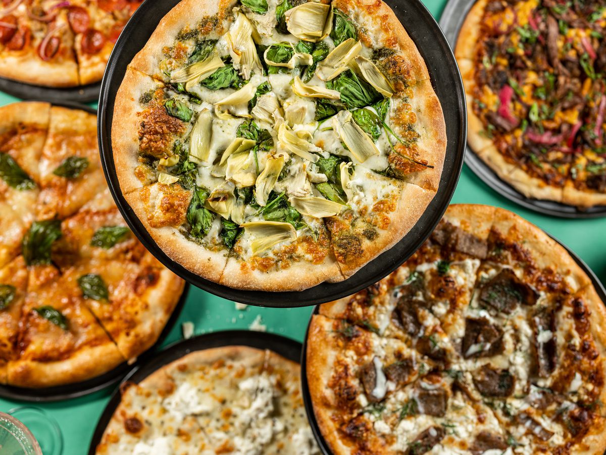 A green tabletop holds various pizzas.