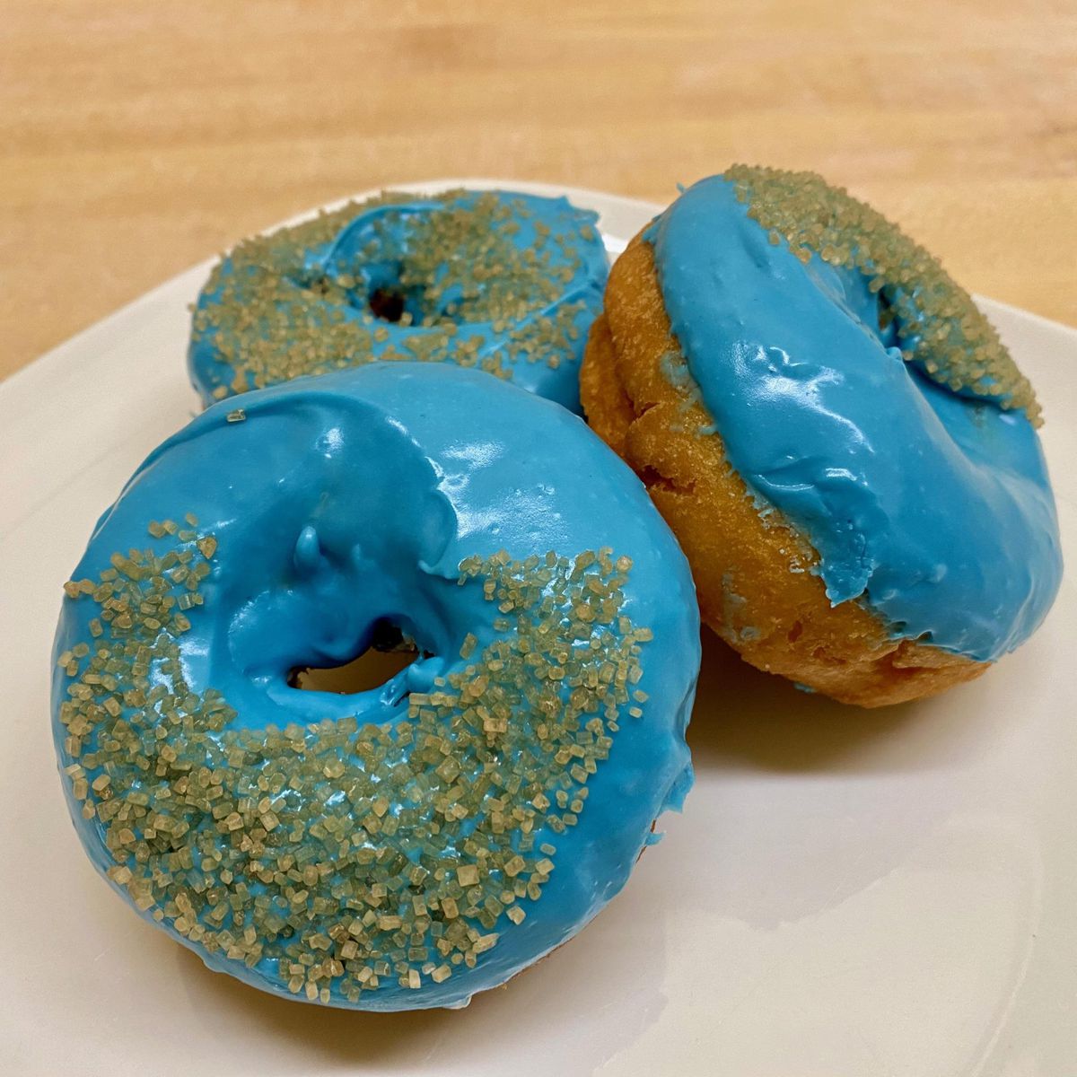 Three blue-frosted and sugared donuts on a white plate.