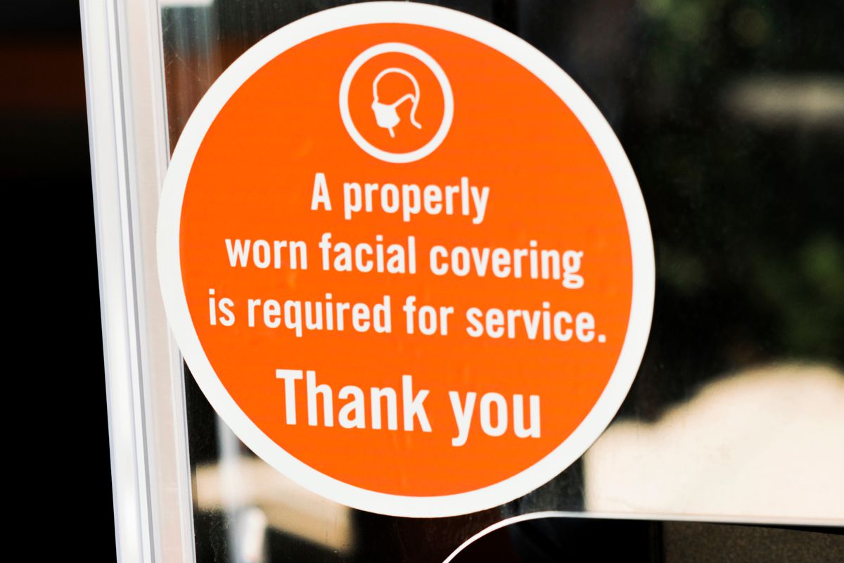 An orange sign on a storefront window says “A properly worn facial covering is required for service. Thank you”