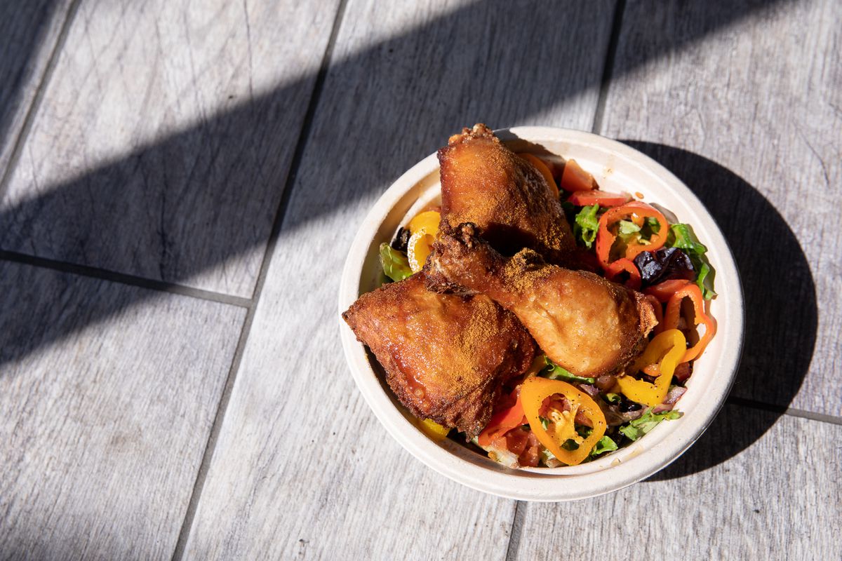 Three pieces of golden fried chicken in a paper bowl filled with salad and sliced red and yellow peppers. 