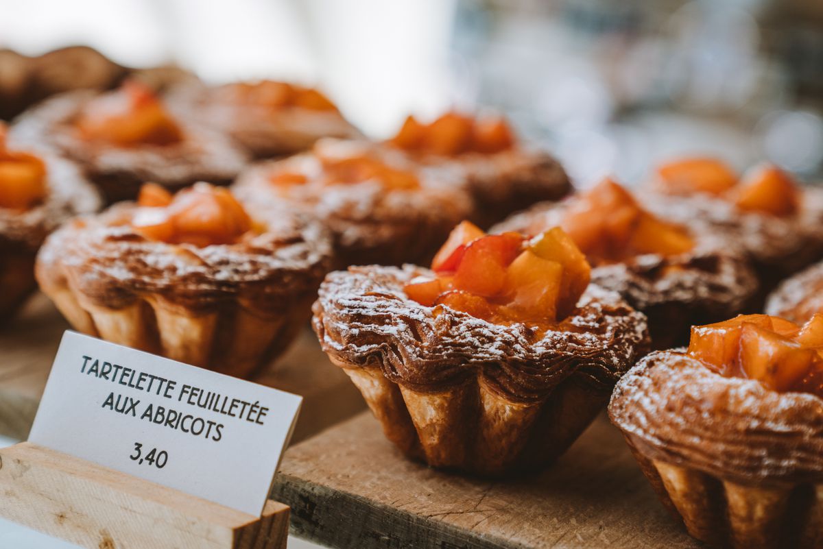 Layered tartlets topped with apricot slices on display with a small lettered sign in French indicating the price, 3,40.