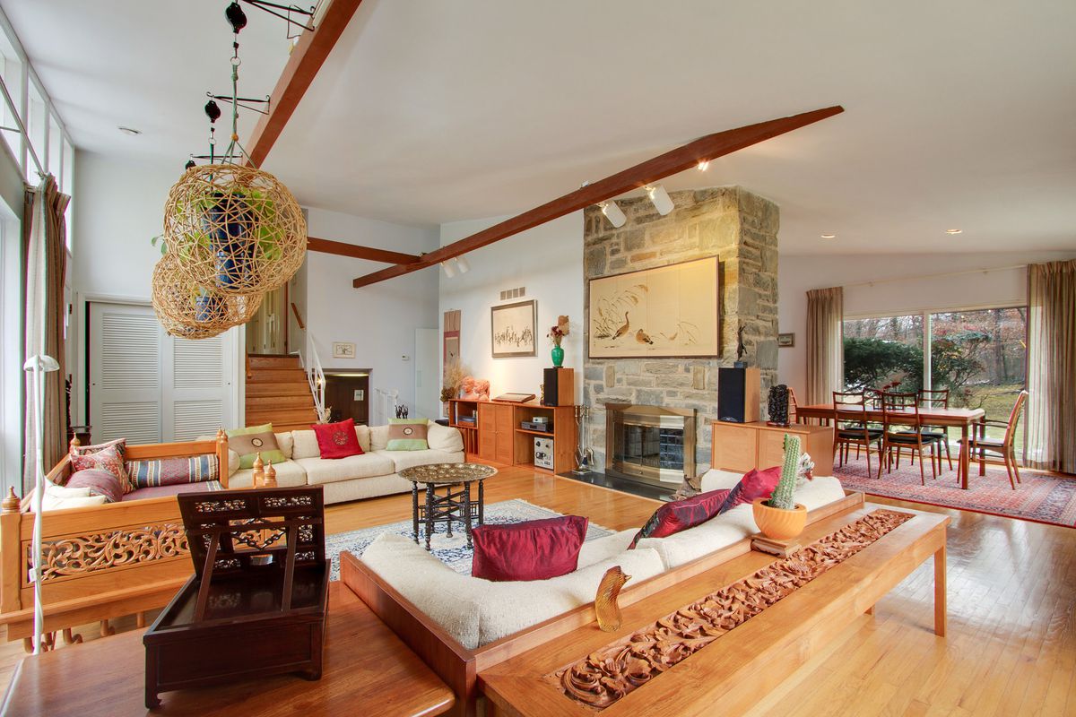 A large living room with vaulted ceilings, a wall of windows, a floor-to-ceiling fireplace, and exposed beams.