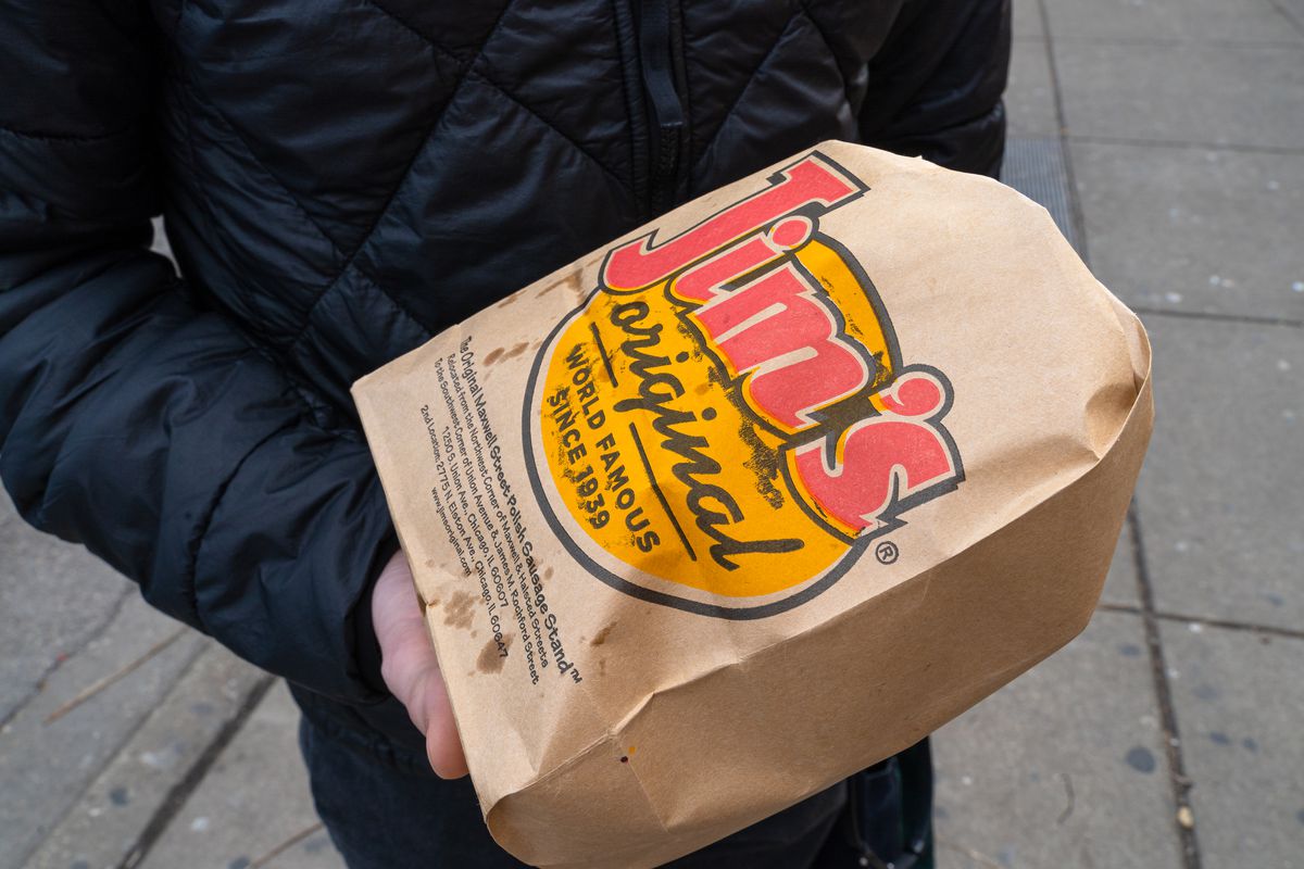 A person holds a brown paper bag with a big red and yellow logo that reads “Jim’s Original.”