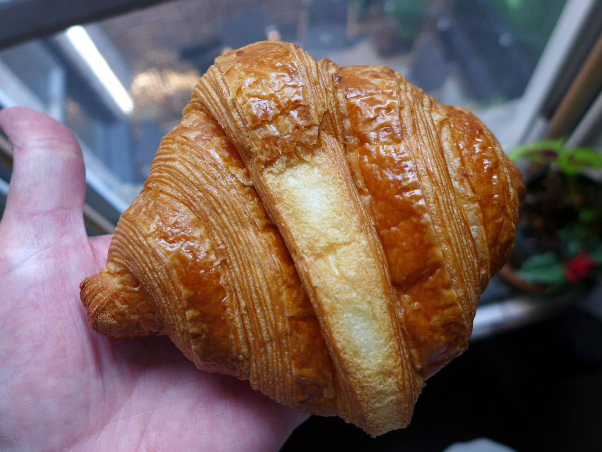 A croissant like a sideways diamond held in the palm of a hand by a window.