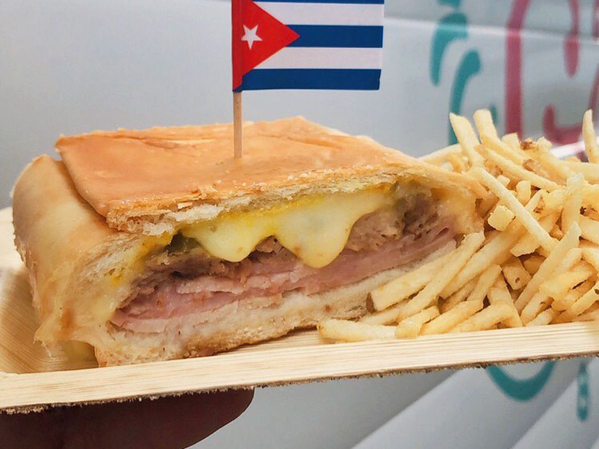 A Cuban sandwich with a Cuban flag on top and a side of fries