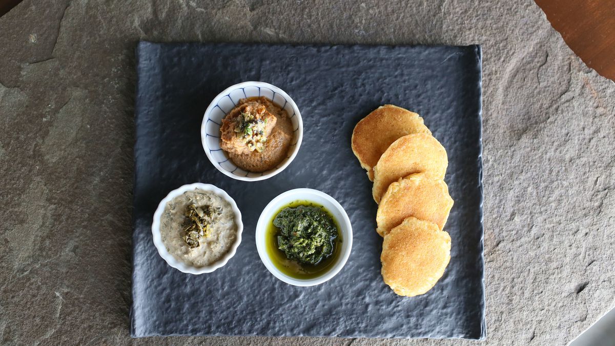Black eyed pea hummus, roasted collard green dip, and zhug (a Yemenese hot sauce) on a plate next to four pieces of bread