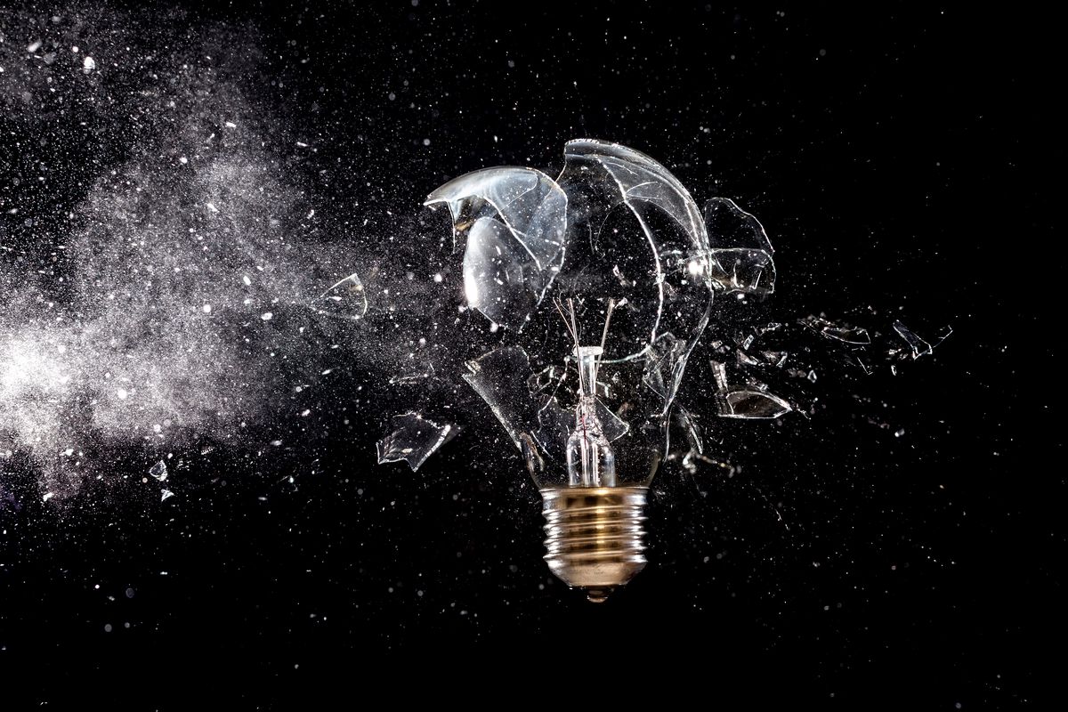 A photo illustration of a lightbulb breaking against a black background.