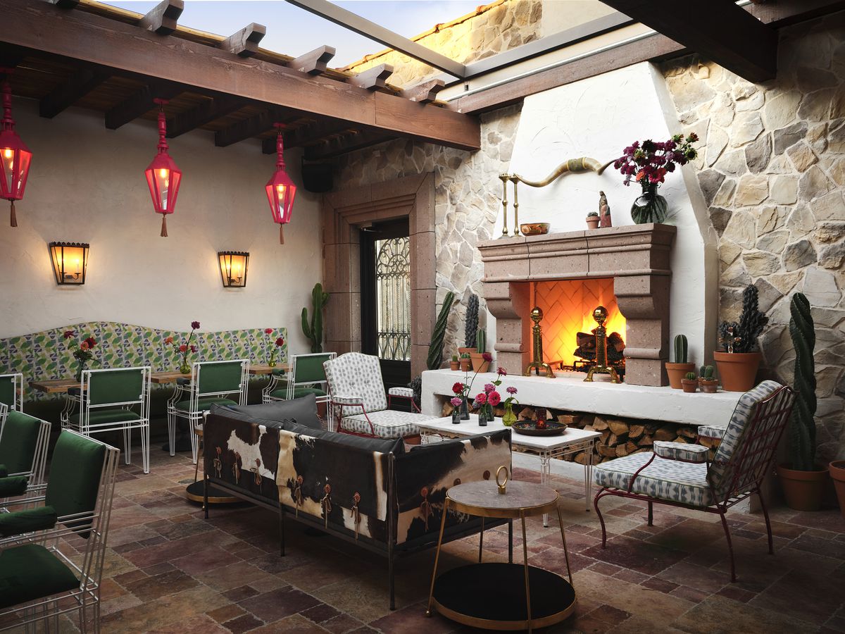 An outdoor patio features a large fireplace, open roof, and mixed furniture.
