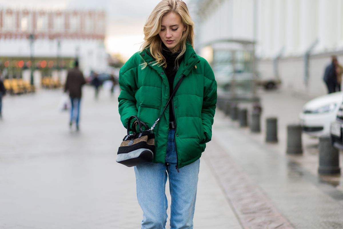 A woman in a green puffer coat, jeans, and a crossbody bag.