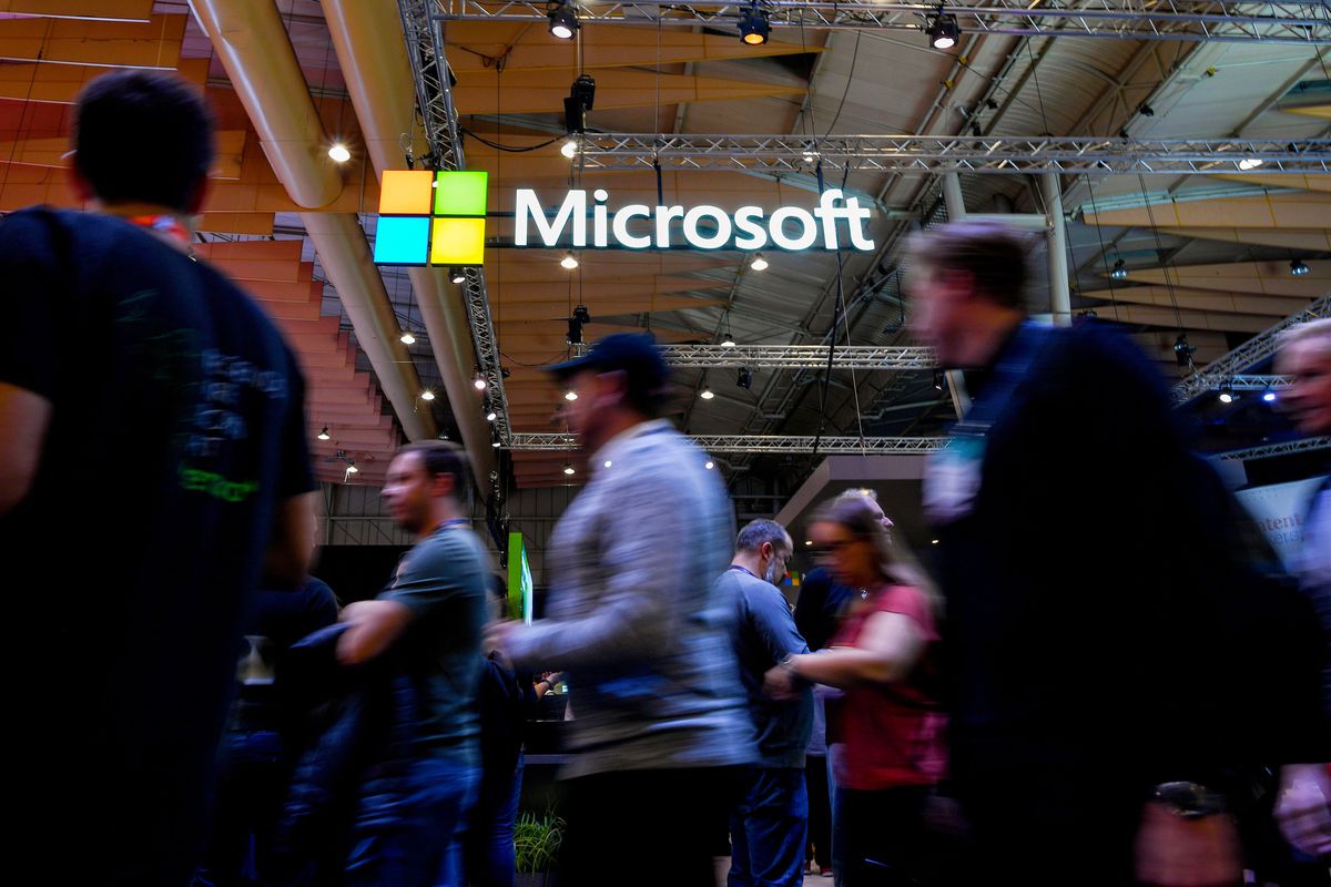 Attendees walk past a sign that reads “Microsoft” and has the four color squares of the Microsoft logo during the Web Summit in Lisbon on November 6, 2019.
