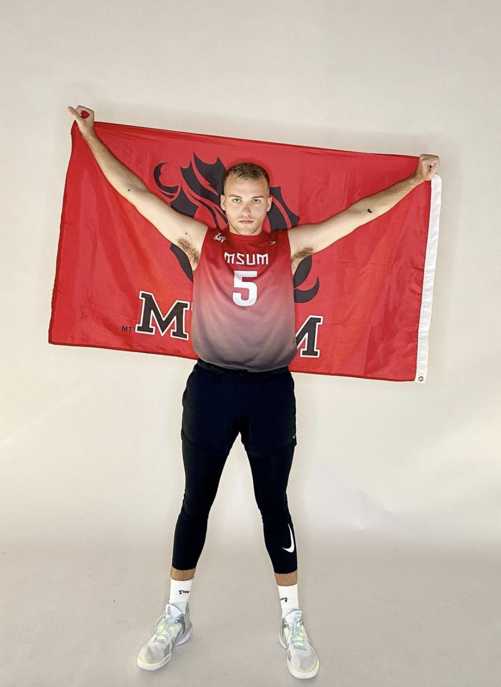 Volleyball player poses with university banner.