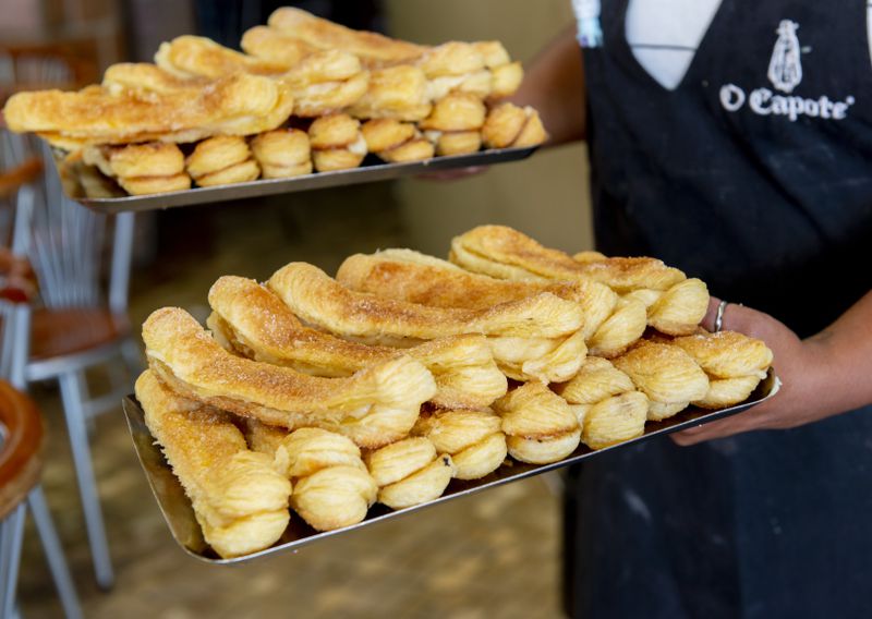 A baker caries trays stacked with multiple rows of pastries.