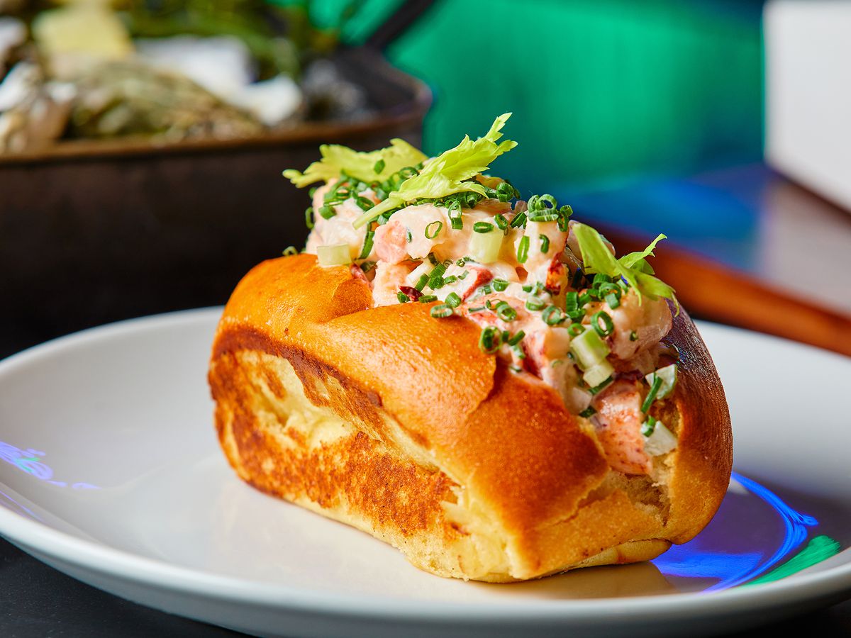 A lobster roll with lobster piled on a toasted bun shown from the side with sprigs of celery leaf on top.