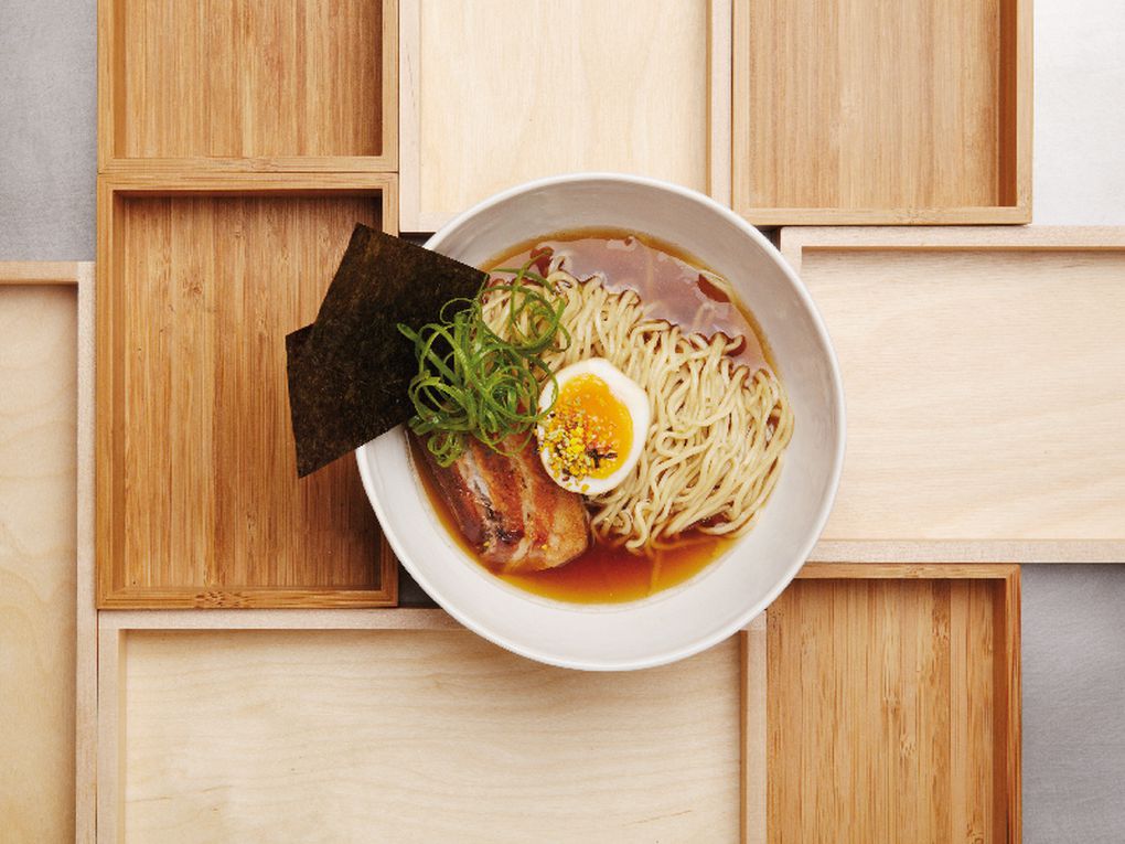 A bowl of ramen seen from above with noodles, egg, greens, slices of pork, and sheets of nori all sticking out of the bowl.