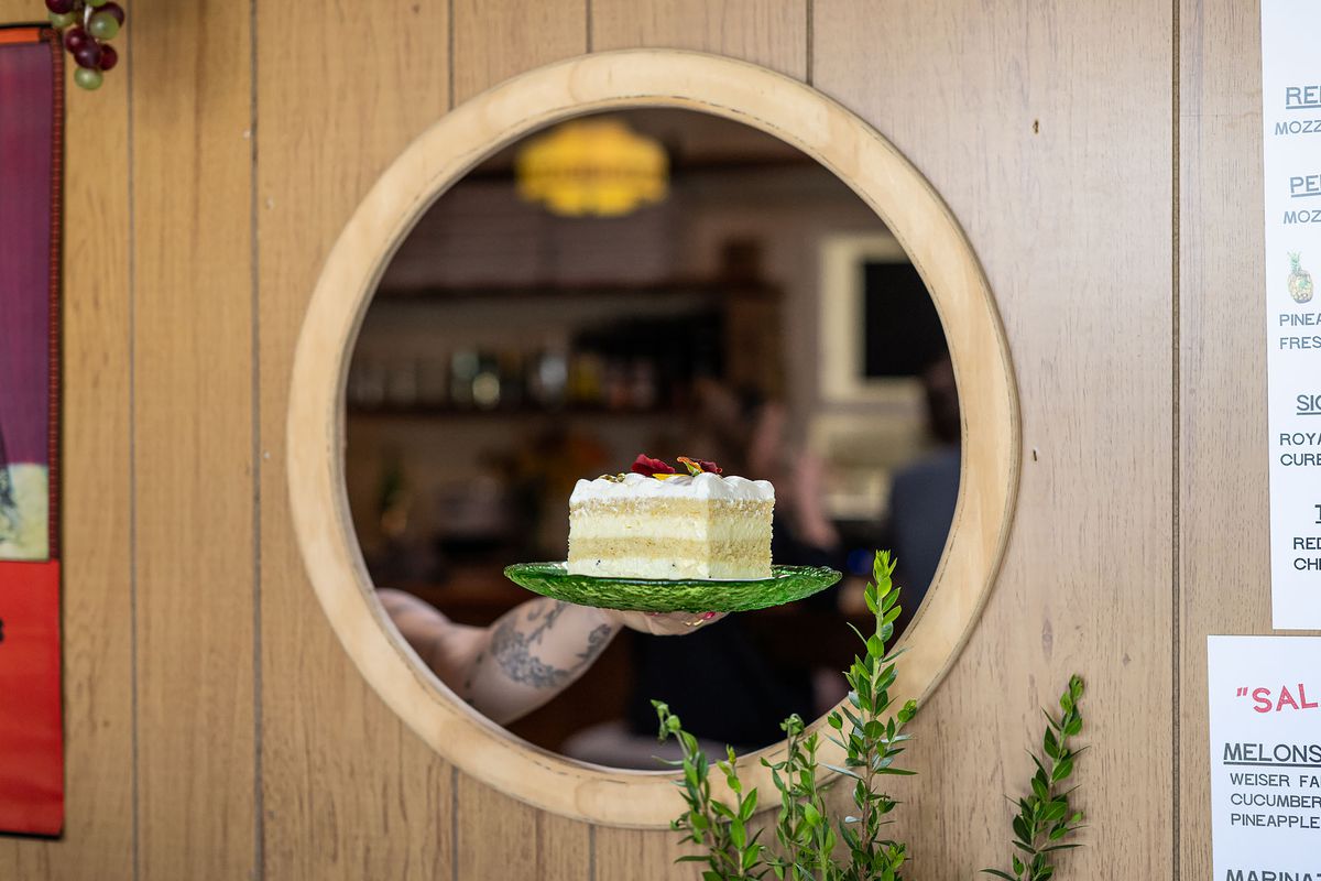 Worker holds a cake through a small circle window at a restaurant.