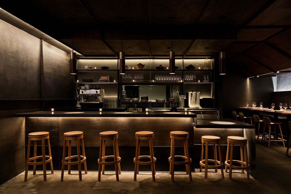 A very dark bar with wooden stools and moody lighting.
